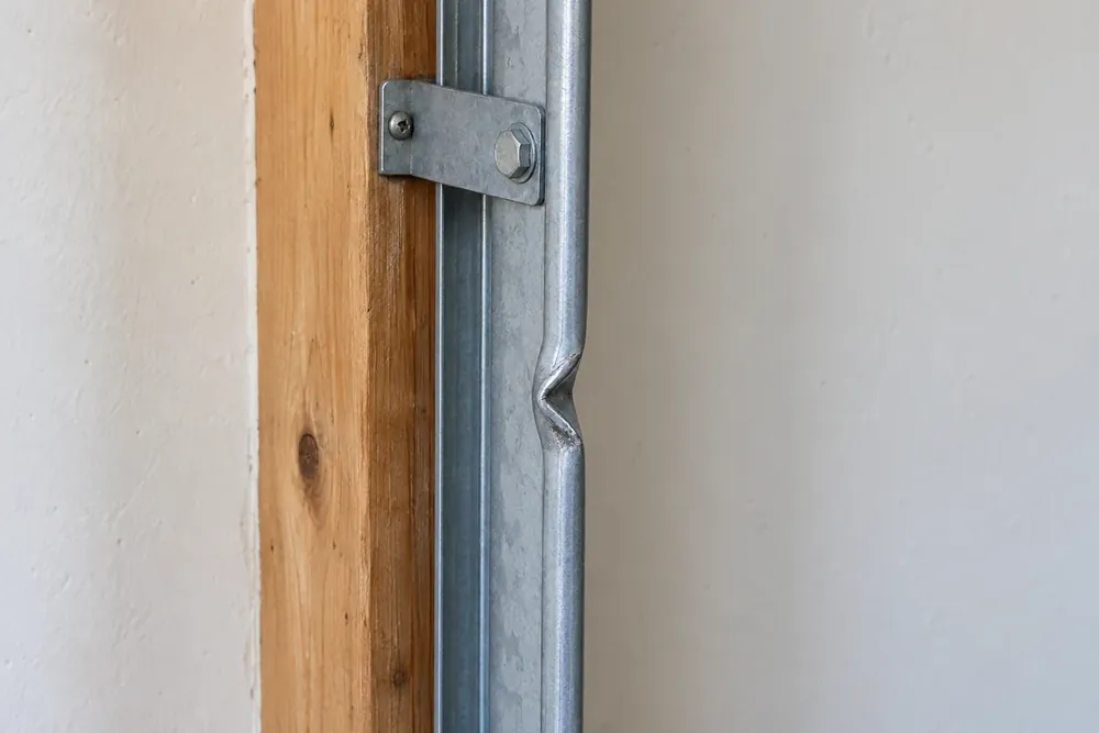 Vertical garage door track with a crushed kink in its rolled edge below a jamb bracket