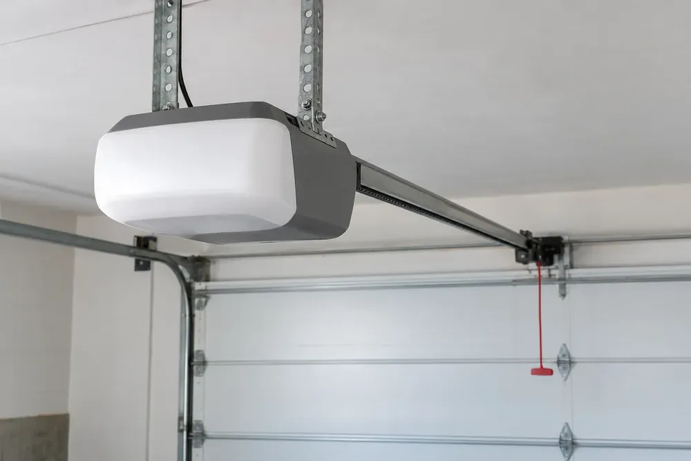 Opener unit on steel ceiling straps with its rail and red release cord above a closed garage door