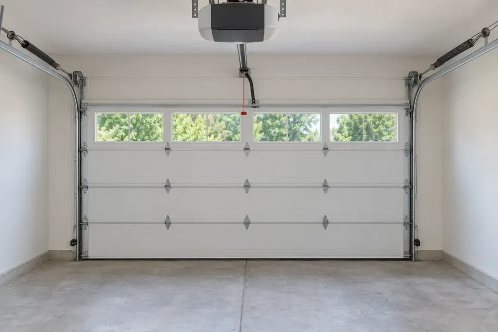 Ceiling-mounted opener with rail, trolley and red release cord above a closed garage door with two floor sensors