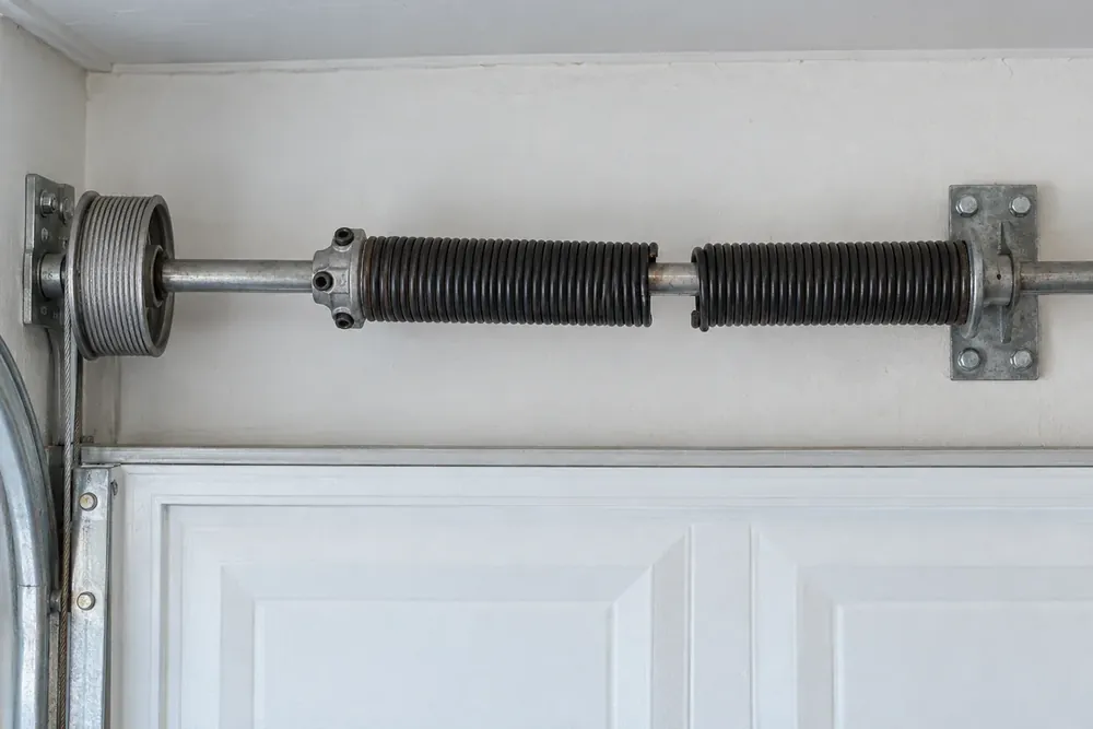 Broken torsion spring on a steel shaft with its winding cone, center bearing plate and cable drum