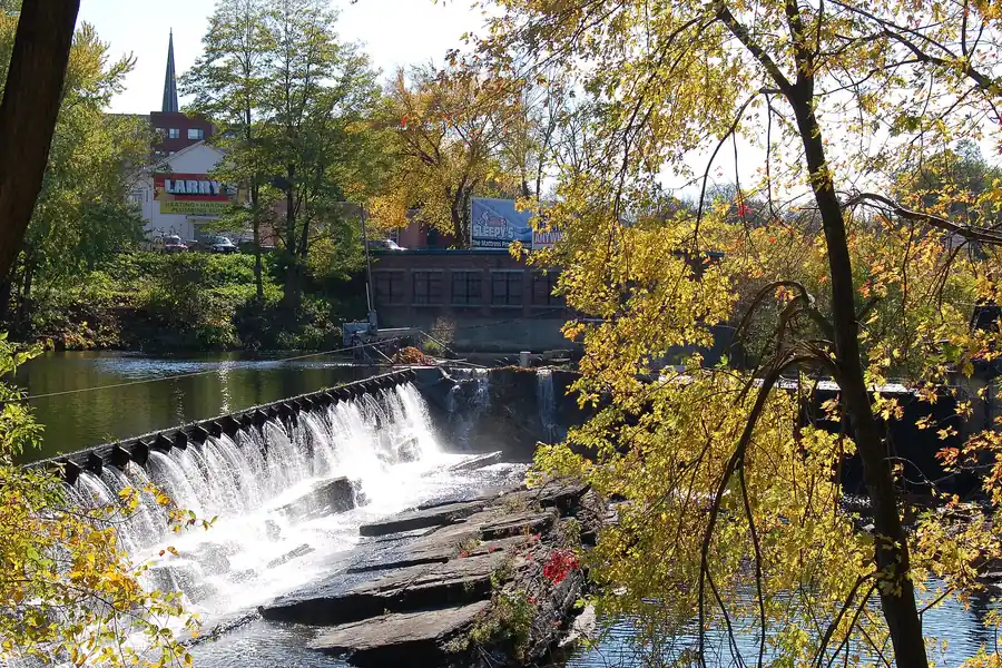 The Chicopee River spilling over a low dam among autumn trees at Chicopee Falls, Massachusetts