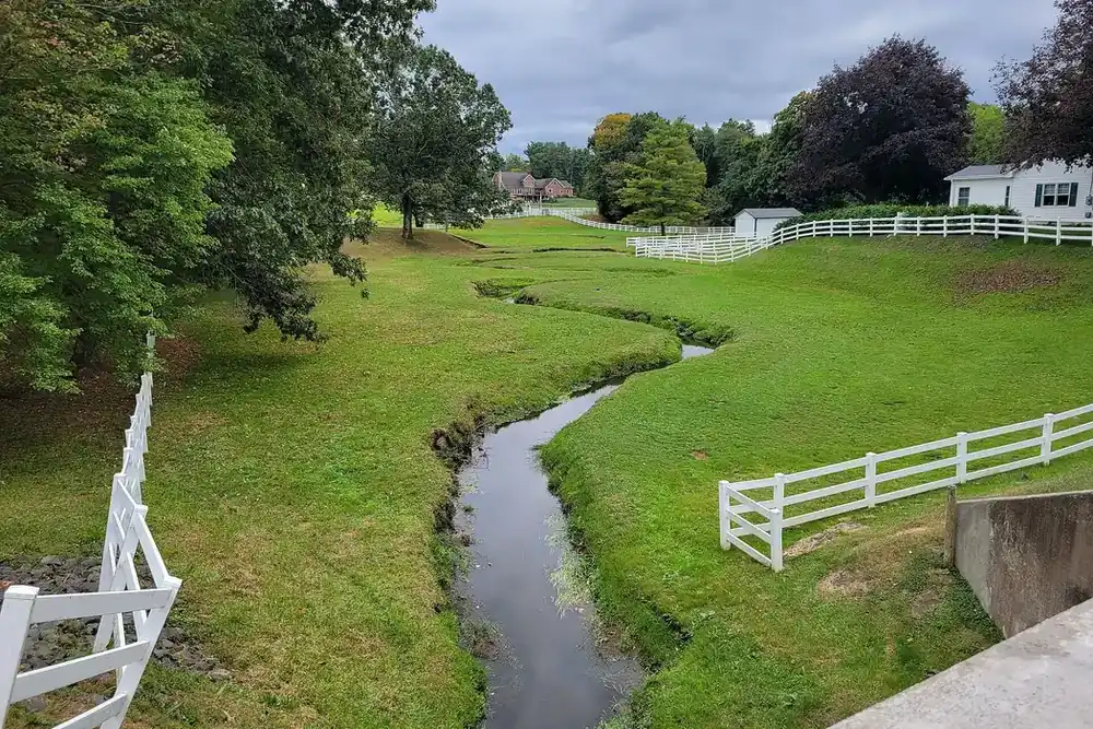 Stoughton's Brook winding between grassy banks and white fences in South Windsor, Connecticut